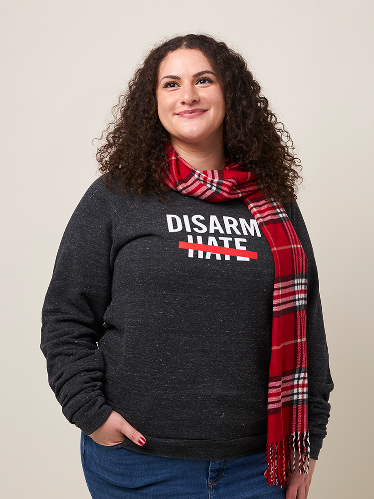 Smiling woman wearing a gray, heathered crewneck sweatshirt with the text DISARM HATE printed in white with a red line through the word HATE.