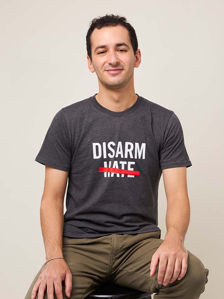 Front view of man wearing a dark gray short sleeve t-shirt with the text DISARM HATE printed in white with a red line through the word HATE.