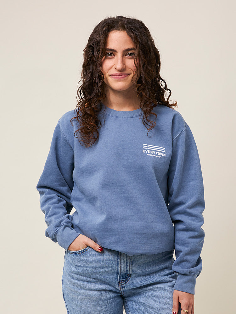 Front view of woman wearing a light blue crewneck sweatshirt with a small white Everytown for Gun Safety logo printed on left chest.