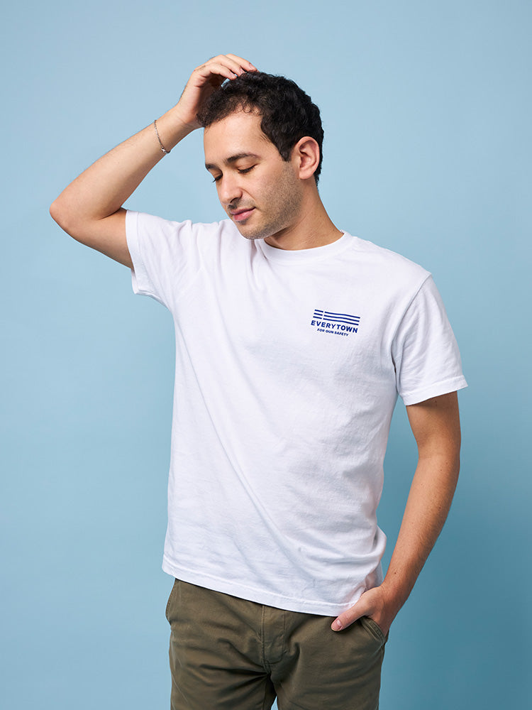Front view of man wearing a white unisex short sleeve t-shirt with a small, dark blue Everytown for Gun Safety logo printed on left chest.