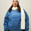 Front view of woman wearing a light blue crewneck sweatshirt with the phrase Keep Going embroidered in white in a cursive font across the chest.
