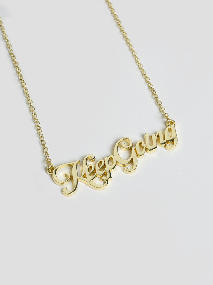 A gold name plate style necklace with the phrase Keep Going in script font.