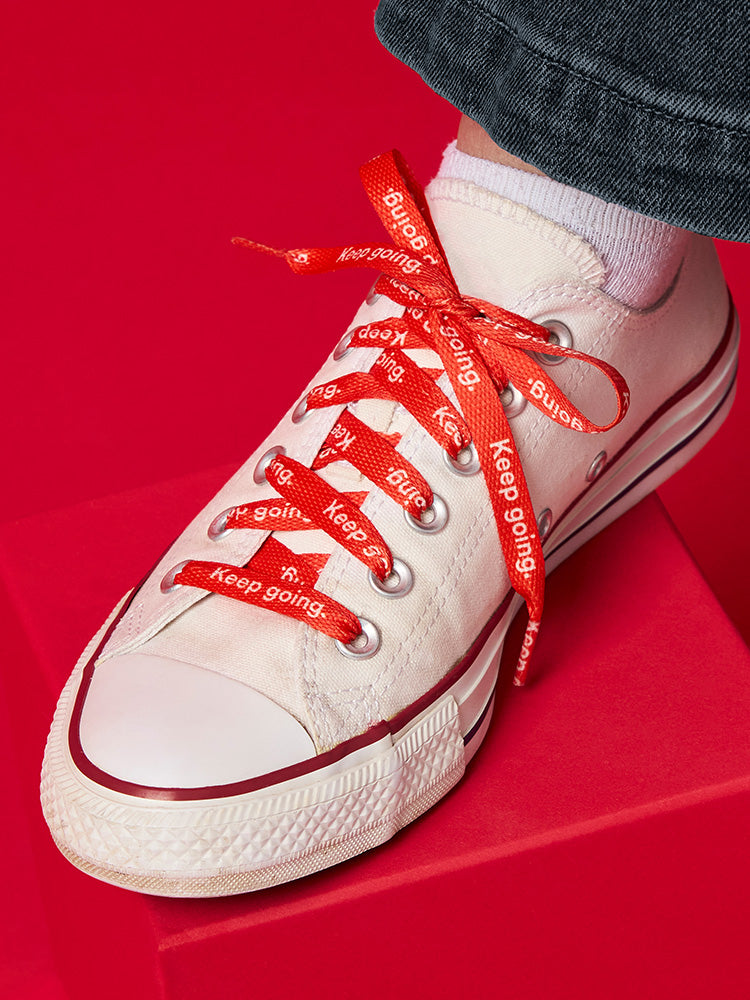 Red shoelaces with repeated white text that reads Keep Going on a white converse sneaker.