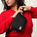 Woman wearing an all black nylon belt bag with an adjustable strap, zip closure, and small white Moms Demand Action Logo printed on the bottom left corner.