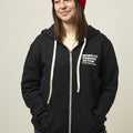 Front view of woman wearing a black zip-up hooded sweatshirt with two front pockets and a small white Moms Demand Action logo printed on left chest.