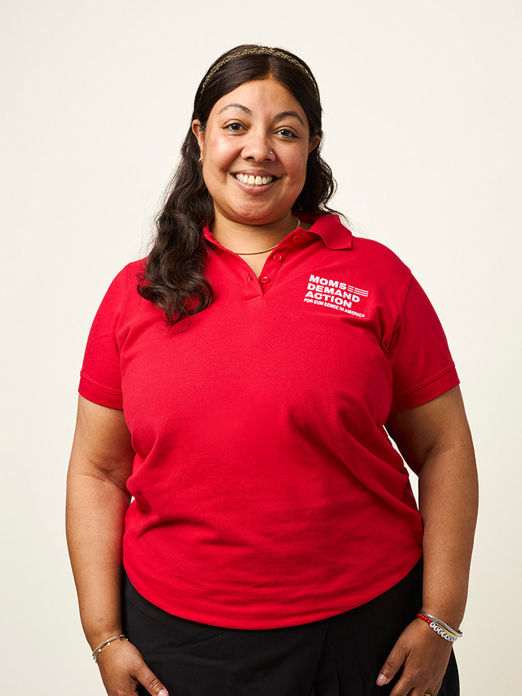Woman wearing a red polo short sleeve shirt with a white embroidered Moms Demand Action logo on left chest.