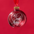 Red, glittery, round plastic ornament with One Tough Mother printed in script font in white on one side.