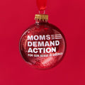 Red, glittery, round plastic ornament with white Moms Demand Action logo printed on one side.