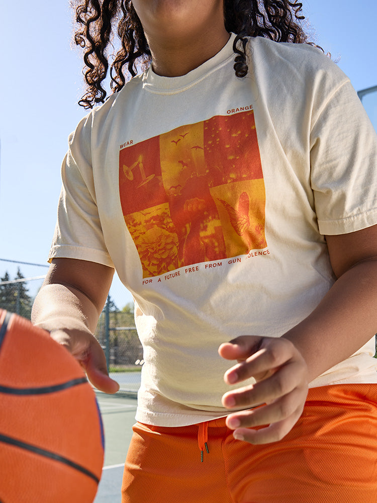 Cream colored short-sleeve unisex t-shirt, front view. There is a 2x3 grid with orange duotone images of candles, birds flying, lanterns in the sky, marigolds, a fist raised, and a monarch butterfly. In small, orange all-caps print, it reads: Wear orange for a future free from gun violence.