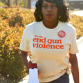 Front of a cream colored short sleeve t-shirt that reads we can end gun violence in bright orange, bold, lowercase letters