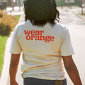 Back of cream colored short sleeve t-shirt that reads wear orange in bright orange, bold, lowercase letters