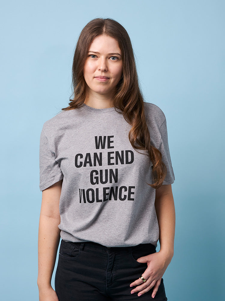 Front view of woman wearing a light gray unisex short sleeve t-shirt with the text WE CAN END GUN VIOLENCE printed in black all caps.